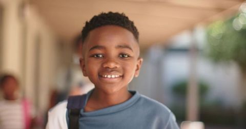 Smiling schoolboy carrying backpack in sunlit campus corridor portrait for back-to-school