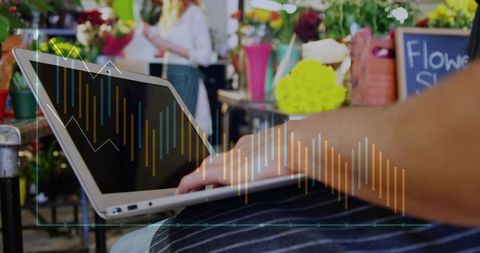 Florist typing on laptop in busy flower shop with sales data overlay and bouquets