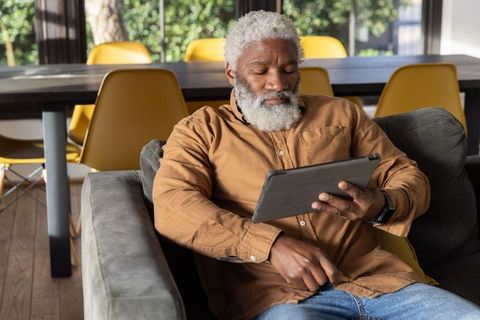 Senior African American Man Relaxing on Sofa and Using Tablet in Bright Modern Living Room