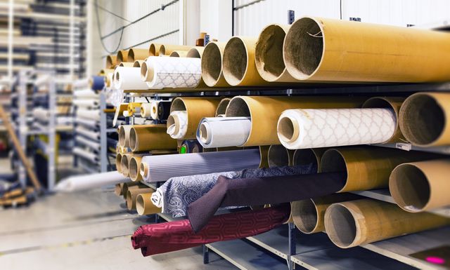 Wide shot of fabric rolls stored on heavy-duty industrial shelves in a modern warehouse. Rolls feature diverse fabric patterns and textures. Ideal for representing manufacturing, textile industry, fabric storage, supply chain, or inventory management concepts.