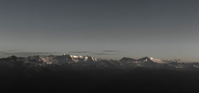 This image captures a majestic mountain range under the twilight sky, providing a dramatic and serene view. The snowy peaks against the dark sky create a stunning visual contrast, making it perfect for use in travel promotion, nature blogs, environmental awareness campaigns, and desktop wallpapers. Ideal for evoking a sense of tranquility, grandeur, and the beauty of natural landscapes.