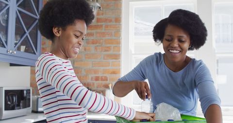 Mother and Daughter Smiling While Recycling in Kitchen