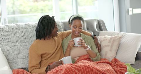 Cozy african american couple cuddling on sofa drinking coffee under rust orange throw