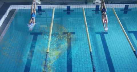 Two female swimmers diving simultaneously into parallel lanes competing in indoor pool