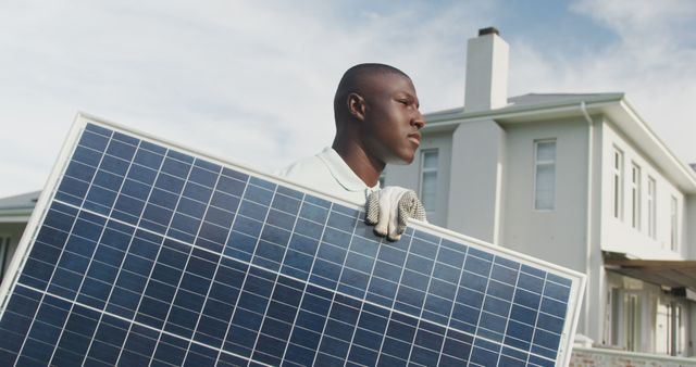 A technician is carrying a solar panel in front of a modern residential home. This image is ideal for illustrating concepts related to renewable energy, sustainable living, green technology, home improvements, and environmental consciousness.