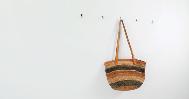 A woven basket hangs on a hook against a clean, white wall, with copy space. Its earthy tones and simple design suggest a minimalist aesthetic or a decluttered lifestyle.