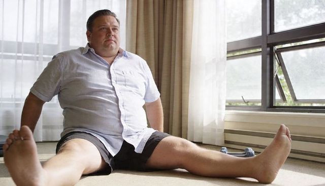 Overweight man resting after gentle home workout with dumbbells by sunlit window on carpet