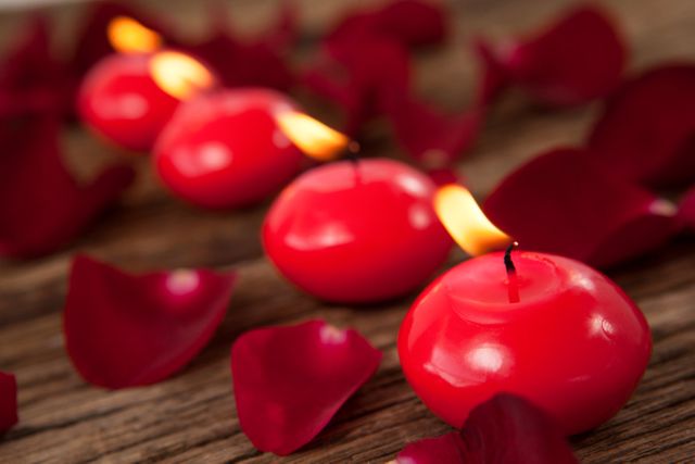 Red wax candles surrounded with rose petals against wooden background