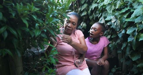 Elderly Woman Mentoring Girl Through Botanical Exploration in Backyard
