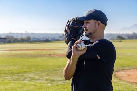 Adult baseball player warming up with ball and glove on sunny suburban field