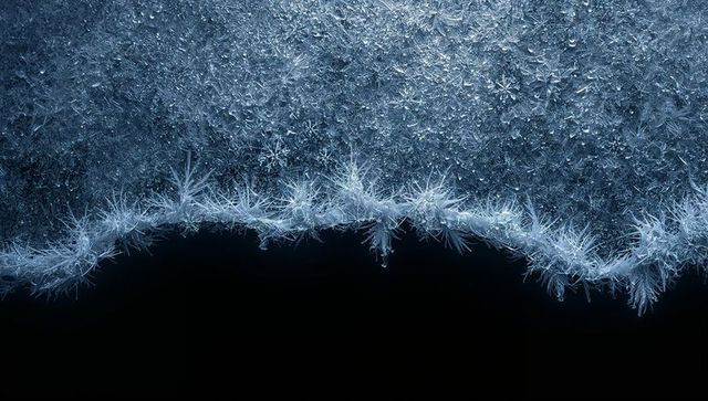 Frost crystals forming jagged icy border on black void macro texture for winter design