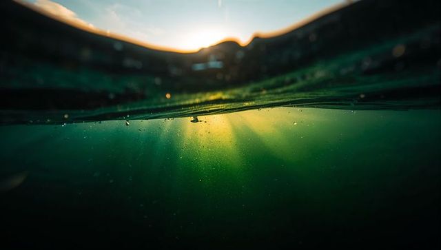 Split waterline revealing sunbeams through green sea water at sunset with backlit droplets