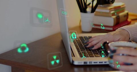 Typing hands holding mug on laptop with green holographic renewable energy icons
