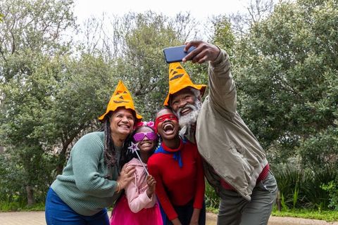 African american family wearing pumpkin hats and costumes taking joyful selfie outdoors