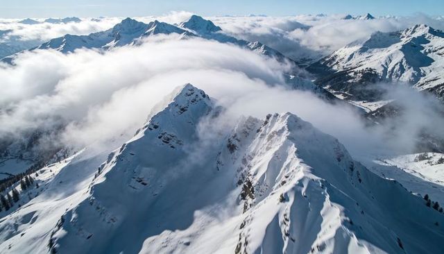 Sunlit Snow Ridge Rising Through Rolling Cloud Inversion Over Alpine Peaks
