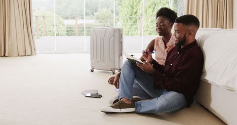 Couple planning travel with tablet and suitcase in cozy bedroom