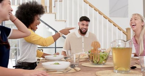 Diverse friends enjoying meal and laughter around table at home