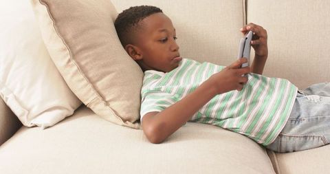 Boy reclining on sofa holding tablet for learning and leisure