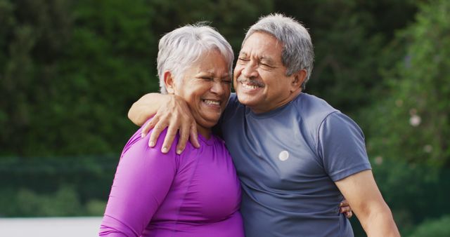 Image of happy biracial senior couple embracing during training on tennis court. active retirement lifestyle, senior relationship and tennis training concept.