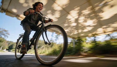 Teen pedaling black commuter bike under canopy, low-angle motion blur, smiling