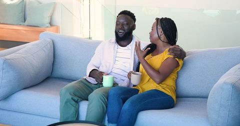 Relaxed Couple Enjoying Coffee and Laughter on Comfortable Sofa