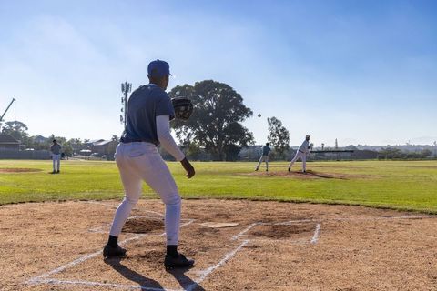 Catcher bracing at plate while pitcher starting delivery on sunlit baseball field