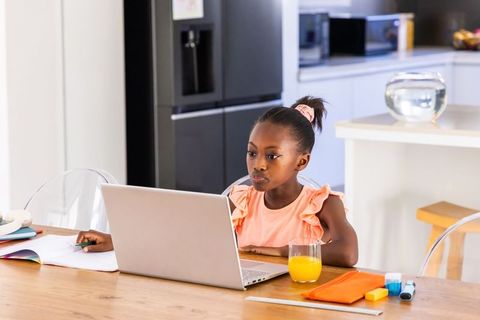 African girl studying on laptop at kitchen table with notebooks and orange juice