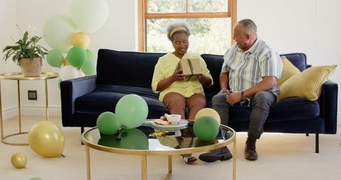 Joyful Senior Couple Exchanging Gifts with Balloons in Living Room