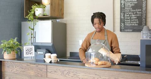 African american barista arranging artisan pastries under glass cloche at cafe counter