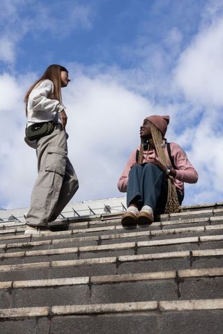 Multicultural friends chatting on stone steps wearing beanie, hoodies, jeans, backpacks