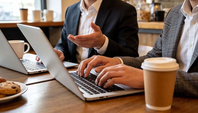 Business professionals typing on laptops in cafe during collaborative meeting with coffee cups