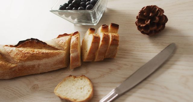 French baguette sliced on wooden table next to bowl of blueberries and knife. Perfect for food blogs, restaurant menus, recipe illustrations, and culinary presentations emphasizing rustic cuisine and fresh ingredients.