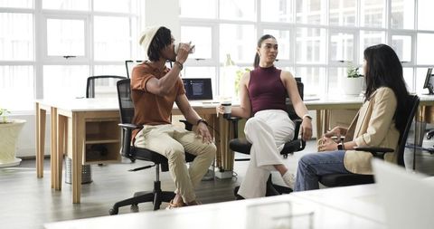 Diverse coworkers collaborating over coffee in sunlit modern open-plan office workspace