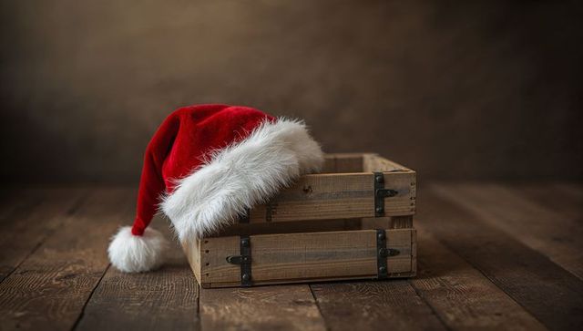 Draping Santa hat over rustic wooden crate on weathered wood planks, cozy Christmas scene