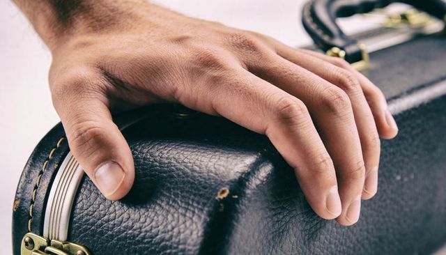 Adult hand resting on worn black leather case with scuffed brass latch