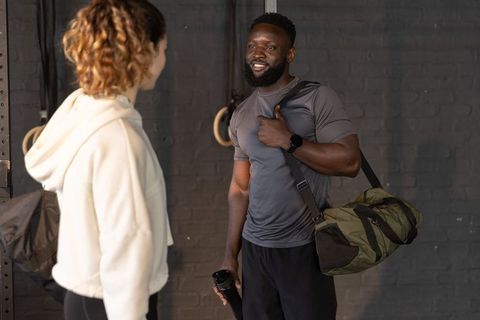 Post-workout gym partners chatting while carrying camo duffel bag and shaker bottle
