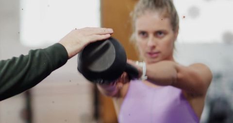 Woman performing kettlebell swing under coach guidance wearing fitness tracker wristband