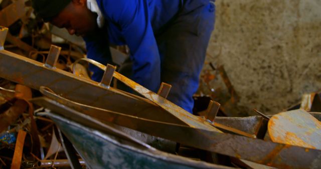 Worker putting metal in wheelbarrow in foundry workshop. Rusted scrap metal pile 4k