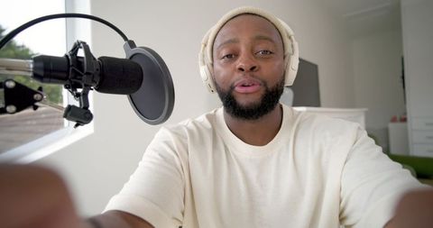 Recording podcast host wearing headphones speaking into microphone in bright home studio