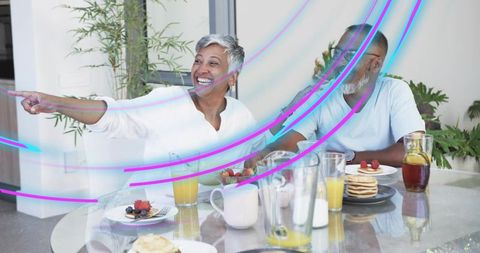 Mature couple sharing joyful breakfast in modern home, woman pointing, candid moment