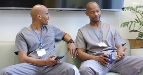 African american male healthcare staff chatting in breakroom wearing gray scrubs