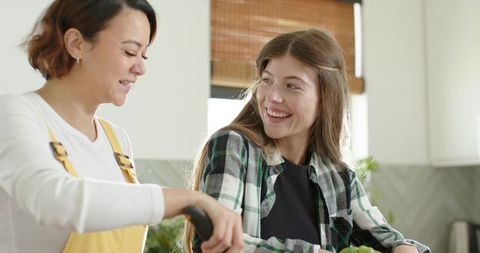 Diverse friends preparing fresh salad together in bright sunlit home kitchen smiling