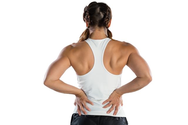 Rear view of female athlete suffering from back pain while standing against white background