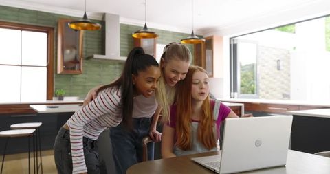 Young Women Leaning Over Laptop Smiling in Modern Kitchen Workspace