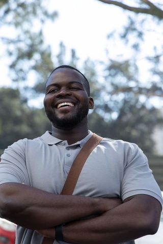 Smiling african american man standing with crossed arms wearing gray polo and brown strap