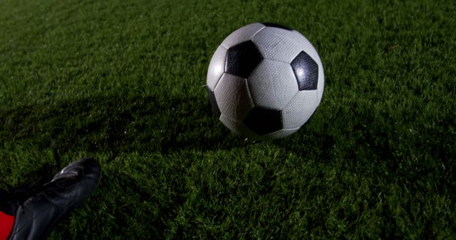Image of a classic black and white soccer ball on a grass field during a night game. Ideal for use in sports-related articles, advertisements, and promotional materials for soccer events or equipment. Can also be used in blogs or websites discussing football training, game techniques, or match reports.
