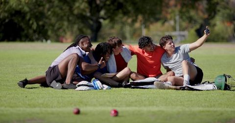 Multicultural men taking joyful selfie on grass after pickup game, celebrating friendship