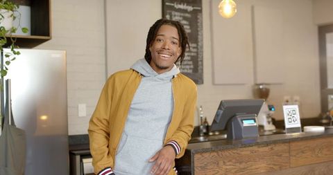 Smiling african american man leaning on modern cafe counter with pos terminal and qr code