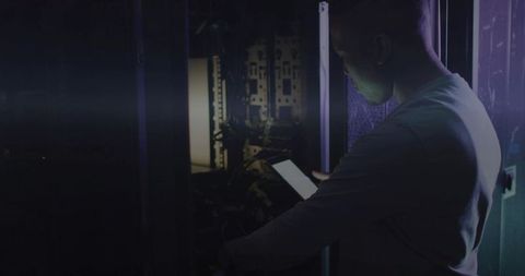 It technician checking server rack with tablet in low-light datacenter cabling maintenance