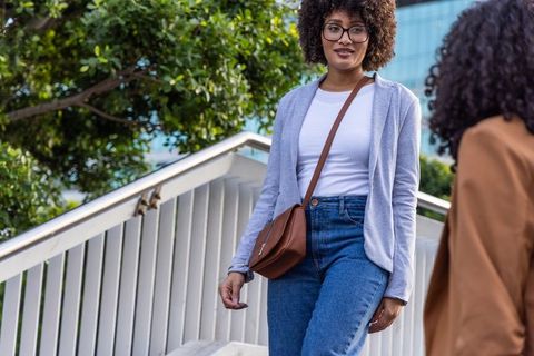 African american woman descending urban stairs carrying brown crossbody bag wearing glasses